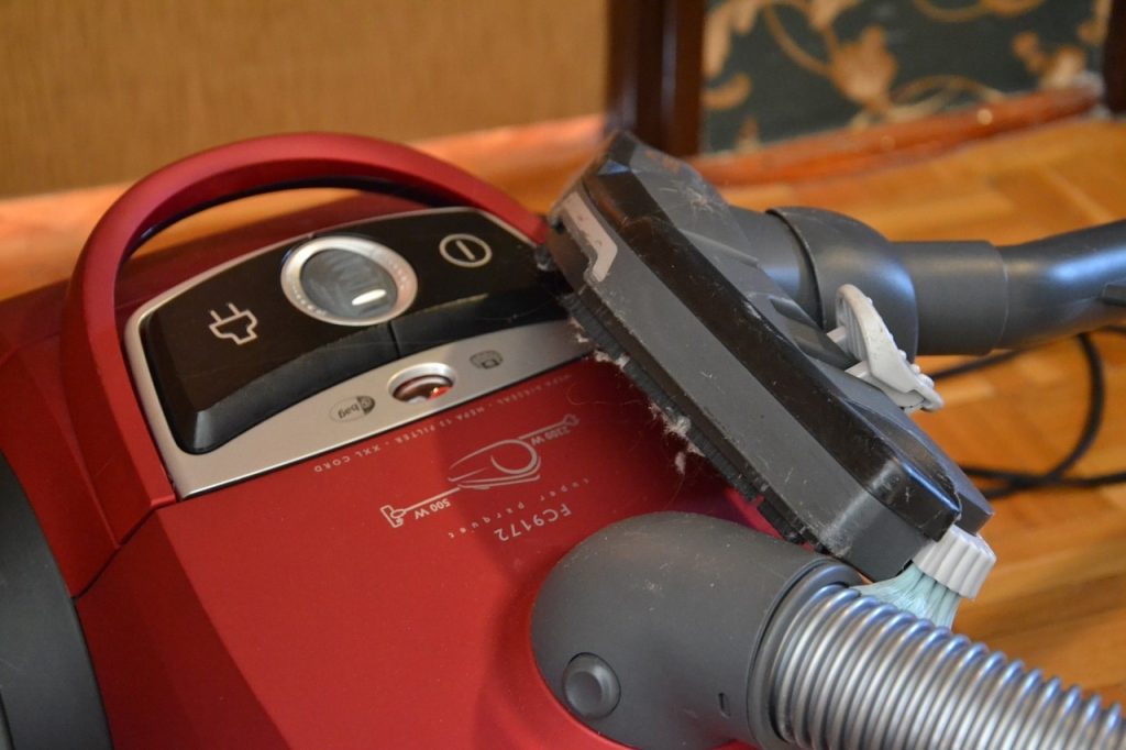 a red vacuum cleaner with a pipe with a brush standing on wooden panels